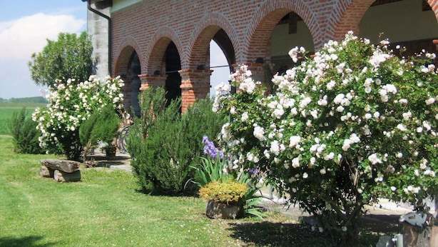 A building with a brick facade and multiple arches. There are flowering bushes and a small garden area in front. - Agriturismo Sesta Presa (Caorle)
