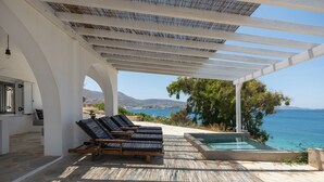 Ett takförsett utomhusområde med solstolar, en swimmingpool och utsikt över havet och bergen.
