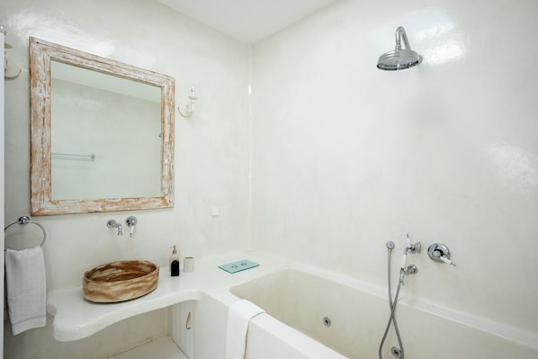 A bathroom with a bathtub, a sink, a mirror, and a showerhead. - Krios Luxury Suites (Paros)