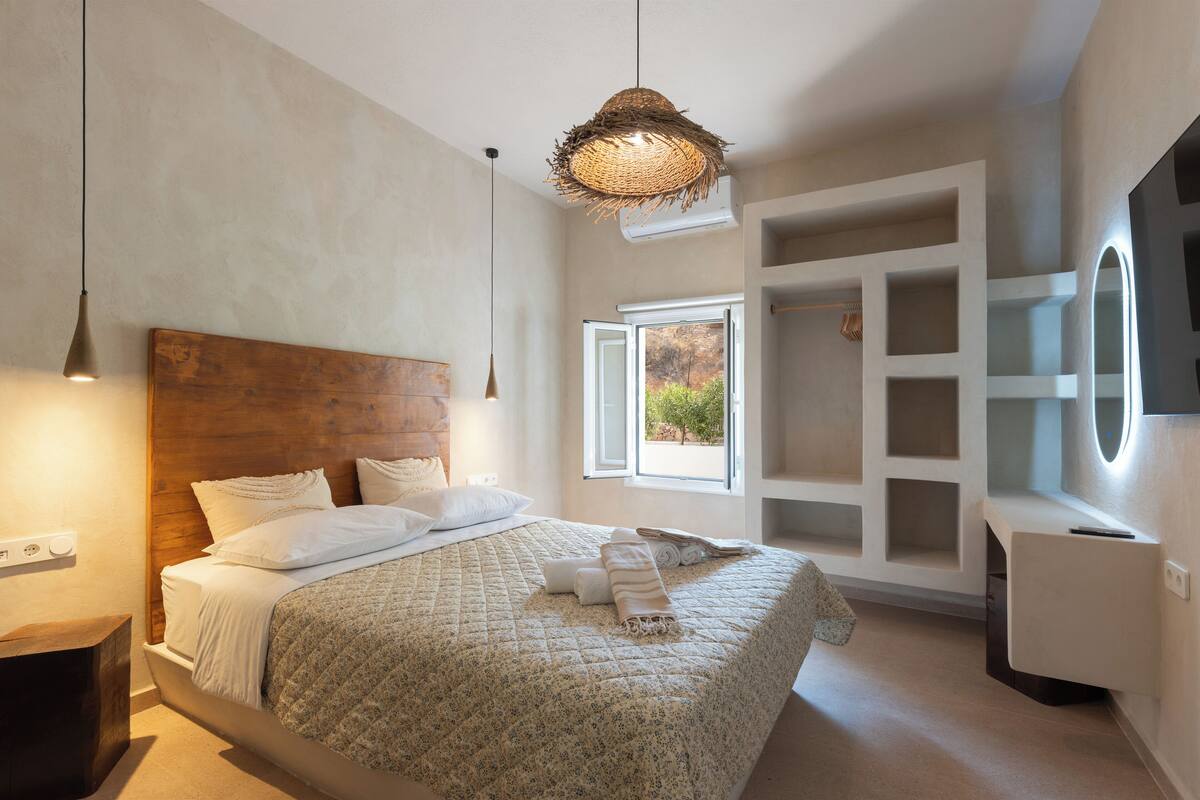 A modern bedroom with a wooden headboard, a large bed with white linens, a hanging woven light fixture, and a built-in TV shelf.