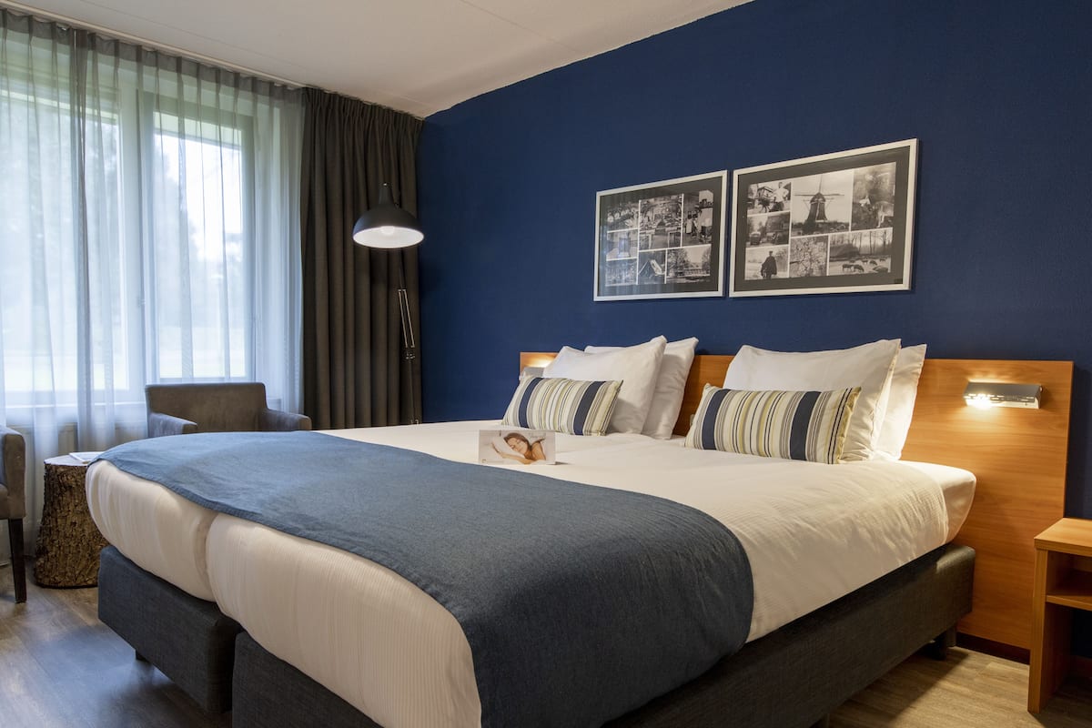 A neatly made bed with a blue and white bedspread, a bedside lamp, and two framed pictures on the wall.