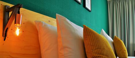 A bed with white and yellow pillows, a wooden headboard, and a wall-mounted light fixture.