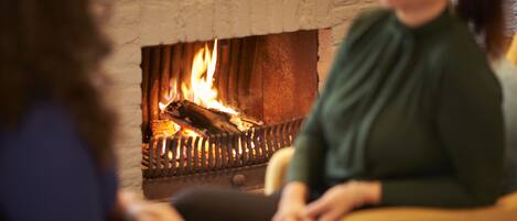 A room with a fireplace, a sofa, and a person sitting near the fireplace.