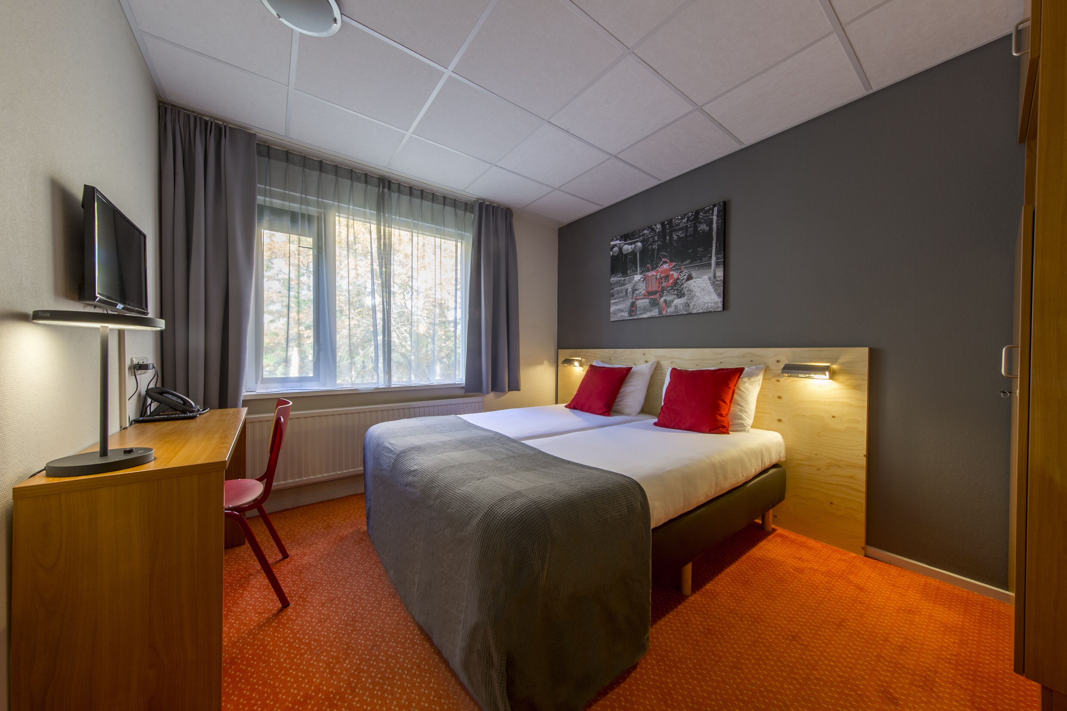 Habitación de hotel con cama, escritorio con silla, televisor y ventana con cortinas.