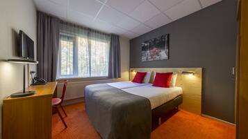 Hotelkamer met een bed, een bureau met stoel, een televisie en een raam met gordijnen.