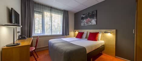 Hotelkamer met een bed, een bureau met stoel, een televisie en een raam met gordijnen.