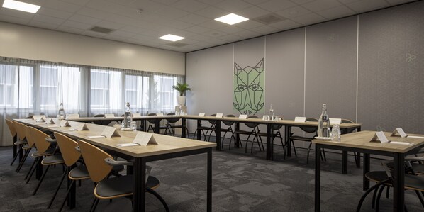 Un salón de conferencias con largas mesas, sillas y una gran obra de arte abstracto en la pared.
