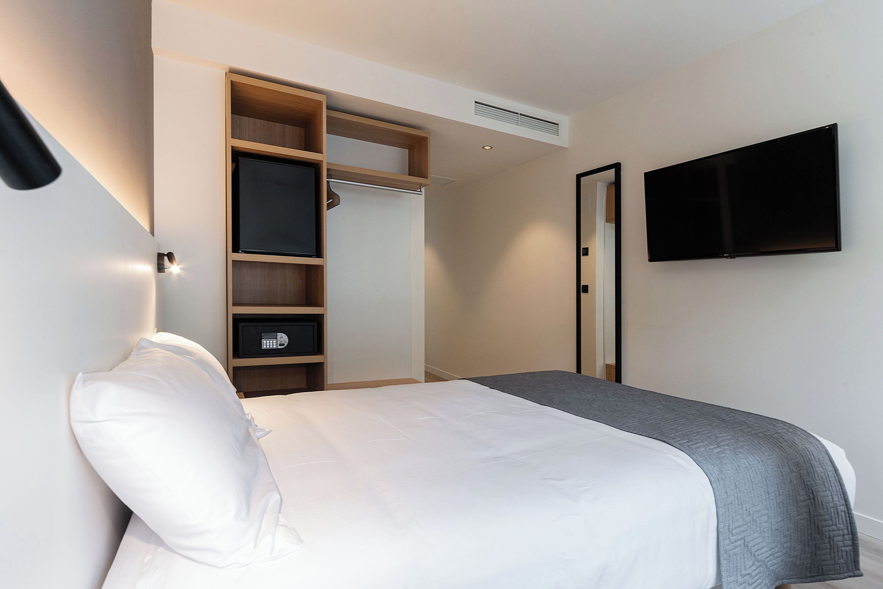 Una habitación de hotel con cama, armario, televisor y caja fuerte.