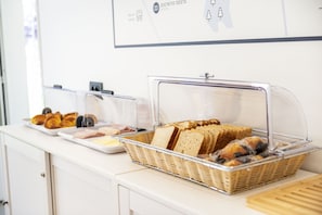 Un comptoir de buffet avec du pain et des viennoiseries présentés dans des récipients transparents.