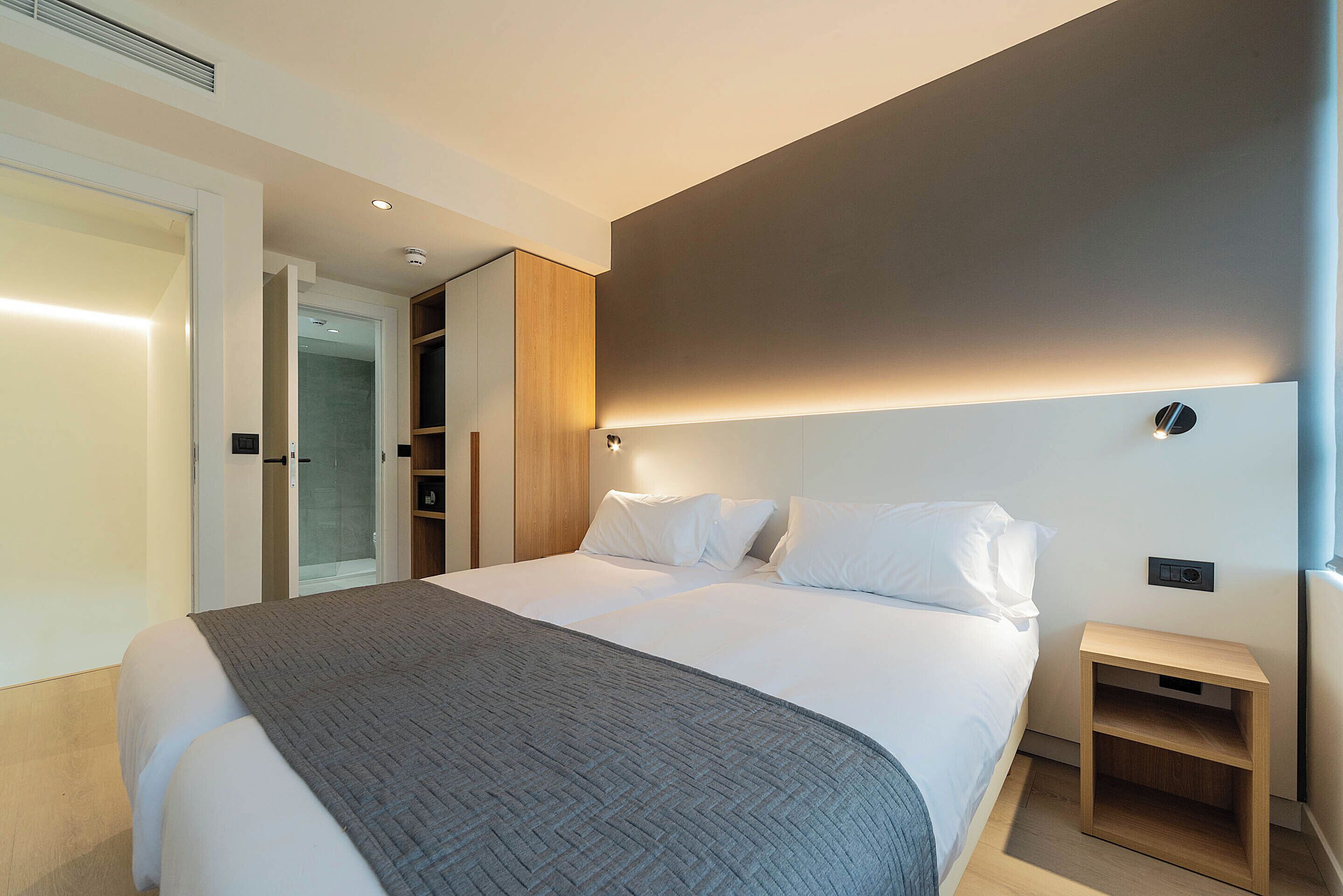 A modern hotel room with a large bed, a bedside table, a wardrobe, and a shower area.
