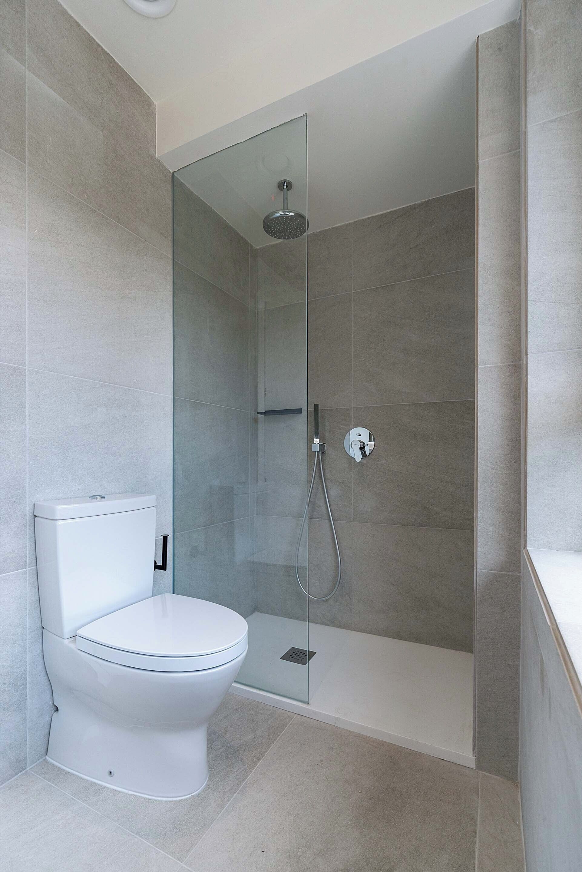 A modern bathroom with a glass-enclosed shower, a white toilet, and a tiled floor.