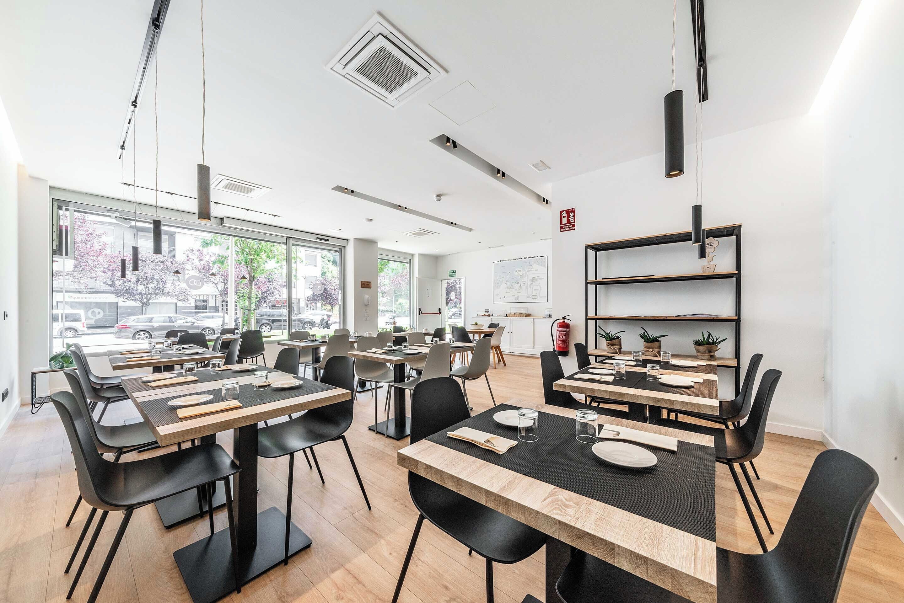 A modern dining area with tables and chairs, large windows, and a fire extinguisher on the wall.