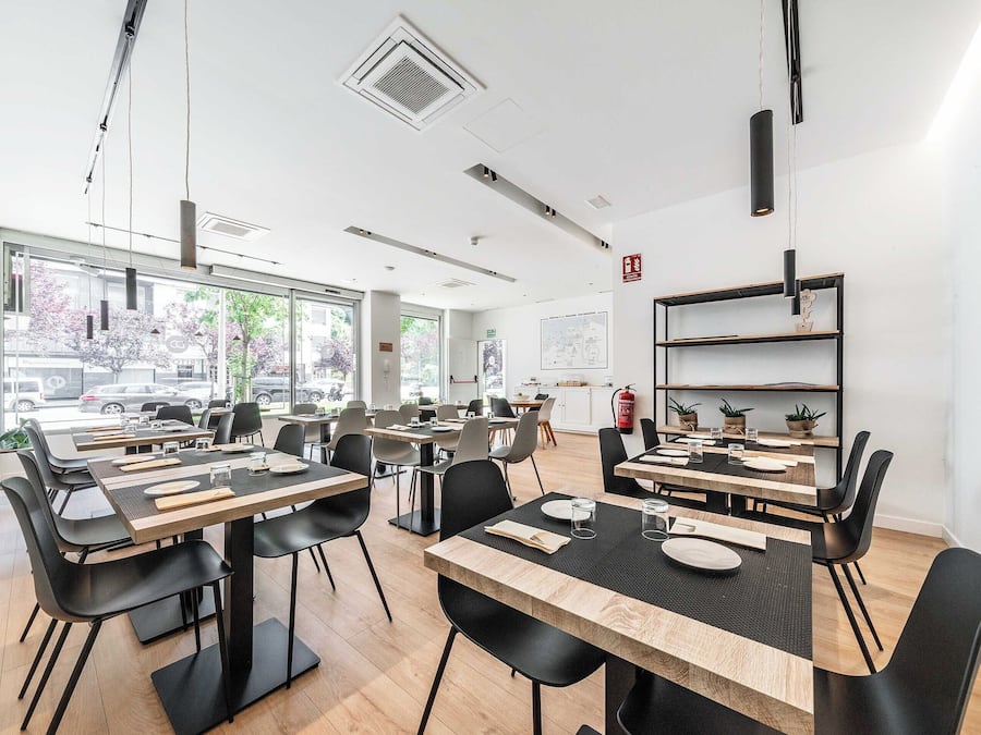 Un comedor moderno con mesas y sillas, ventanas amplias y un extintor en la pared.