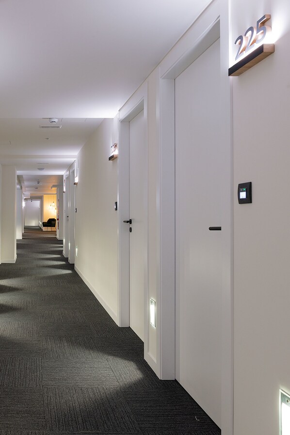A hotel hallway with carpeted floors, white walls, and doors numbered 225. - Hotel Distrito Oeste by Limehome (San Sebastián)