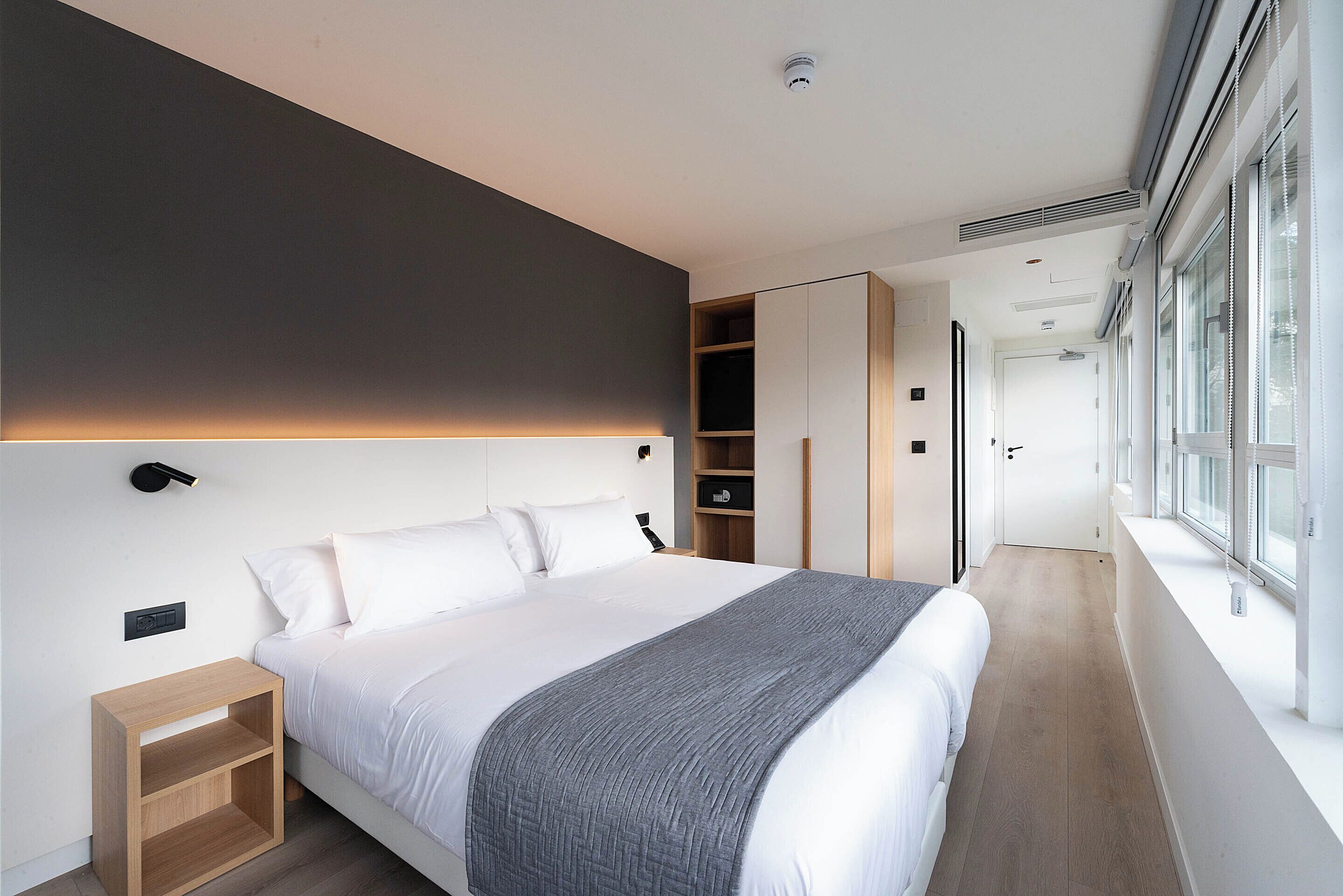 Un dormitorio moderno con una cama grande, mesitas de noche, un armario y una ventana.