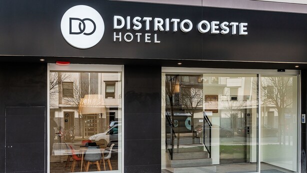 Exterior de l'Hotel Distrito Oeste, amb grans finestres de vidre, façana moderna i entrada visible.