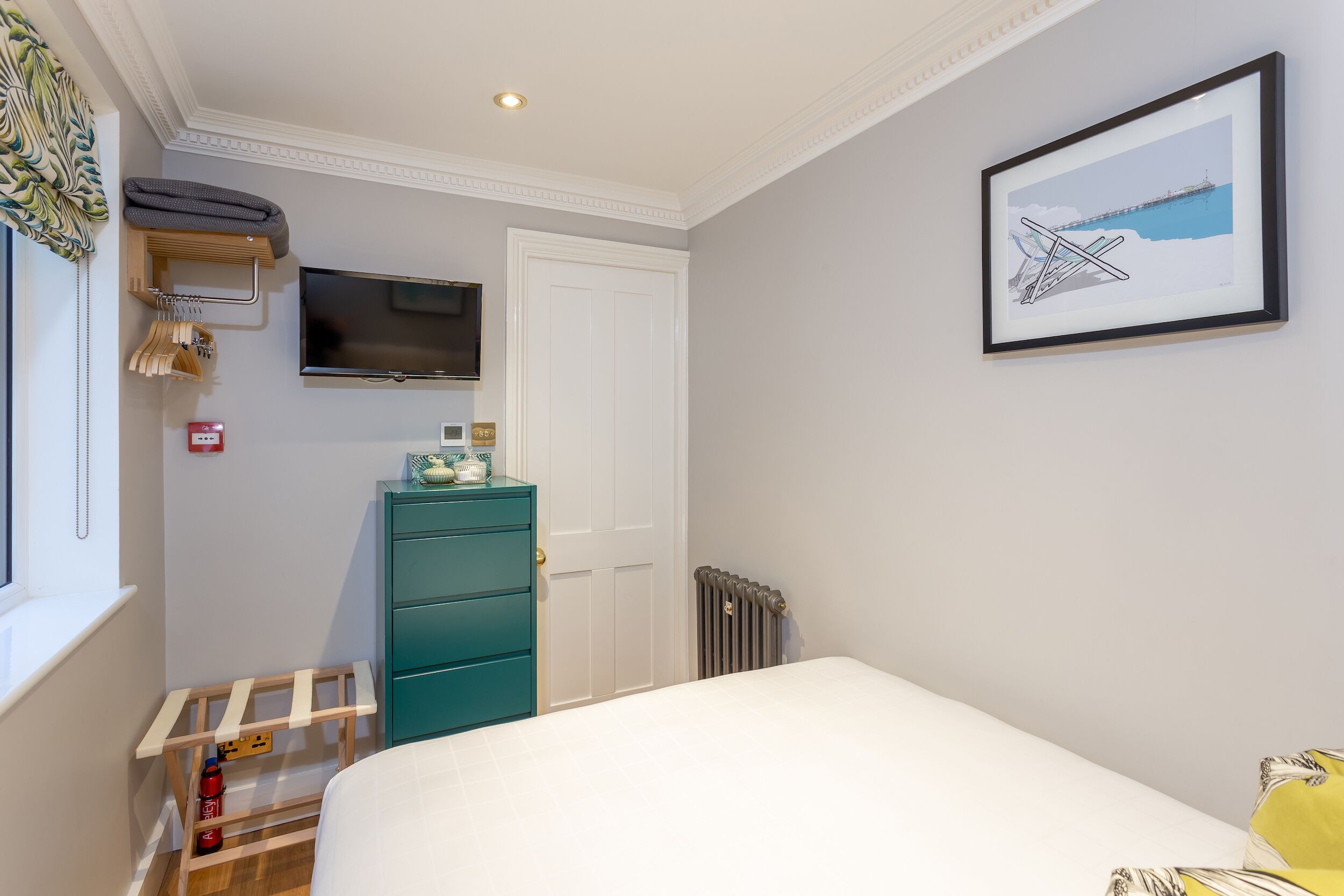Une chambre à coucher avec un lit, un téléviseur fixé au mur, une commode et un tableau encadré.