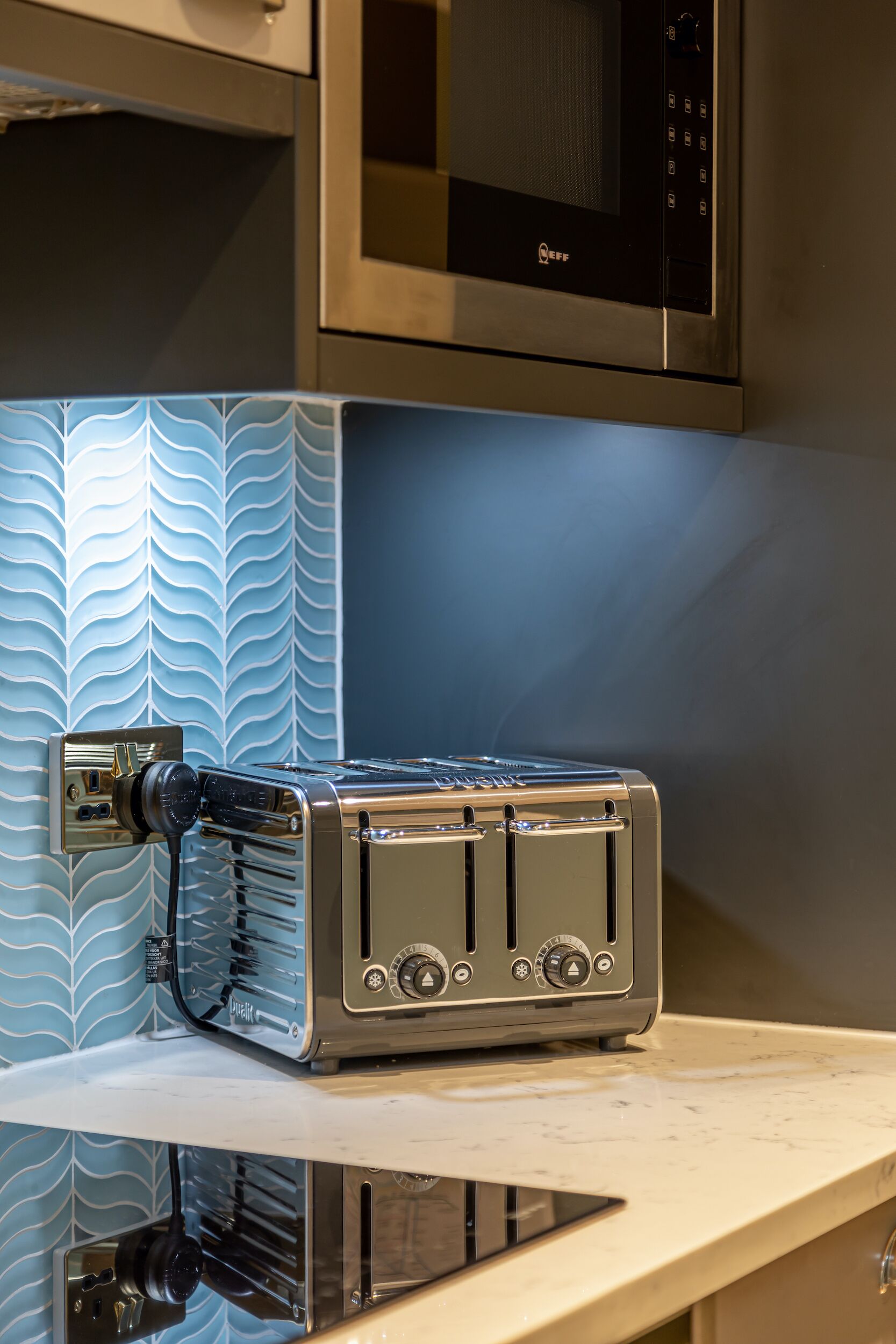 A kitchen with a stainless steel microwave above a patterned backsplash, a toaster on a countertop, and a black induction cooktop below.