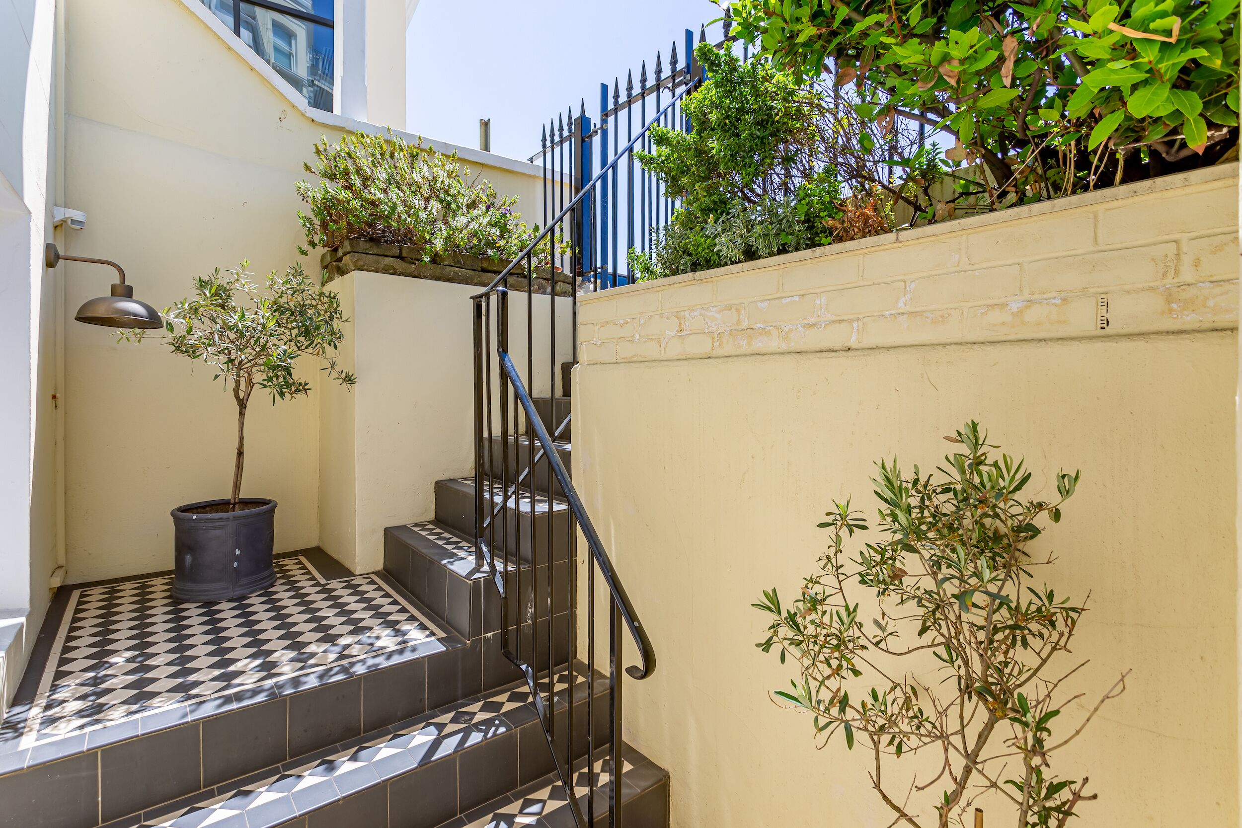 A staircase with black and white checkered tiles, a black metal railing, and potted plants.