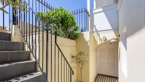A staircase with black railings, a potted plant, and a checkered floor leading to a white door. - Beaches Brighton 1 (Brighton)