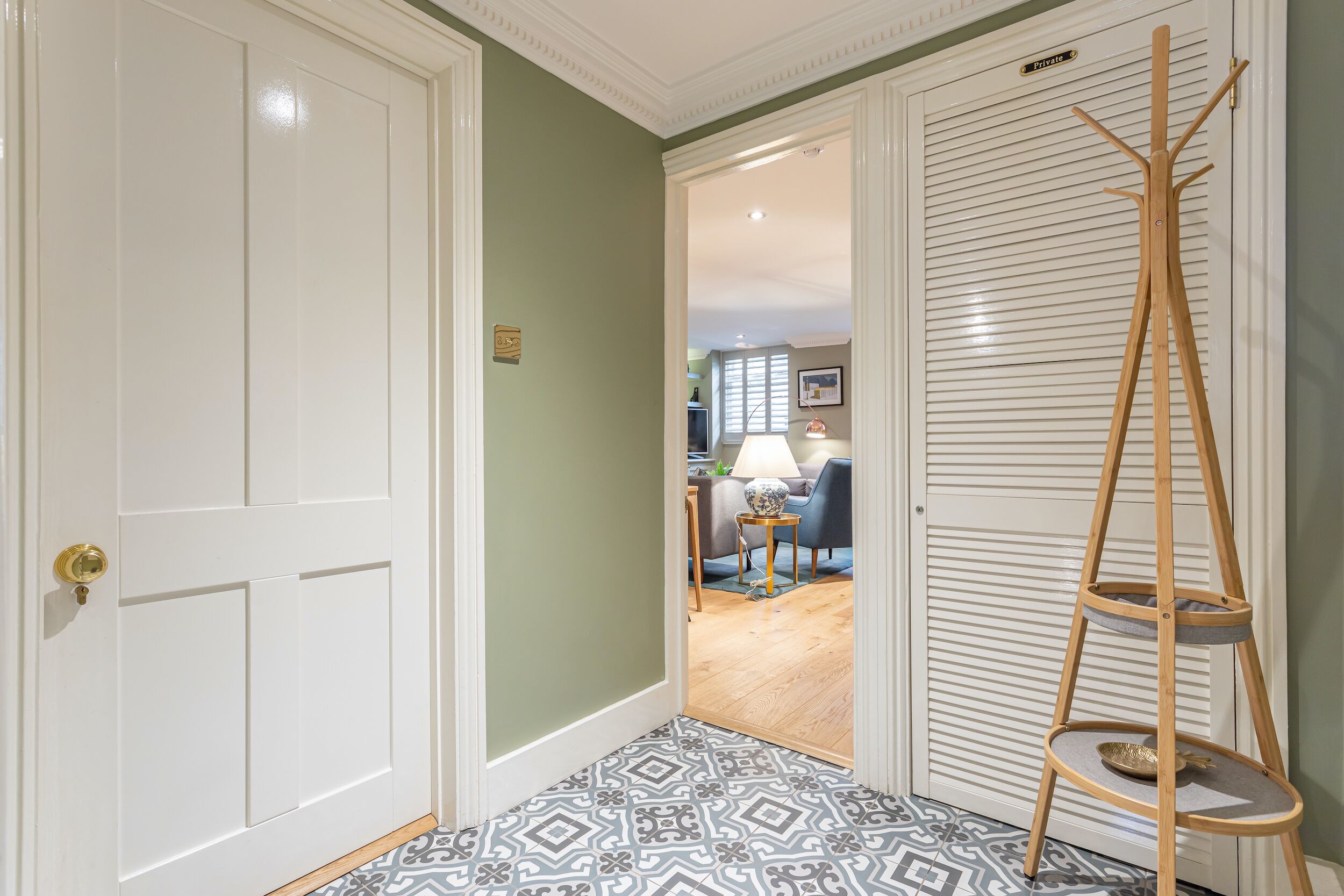 A hallway with patterned floor tiles, a white door, and a wooden coat rack.