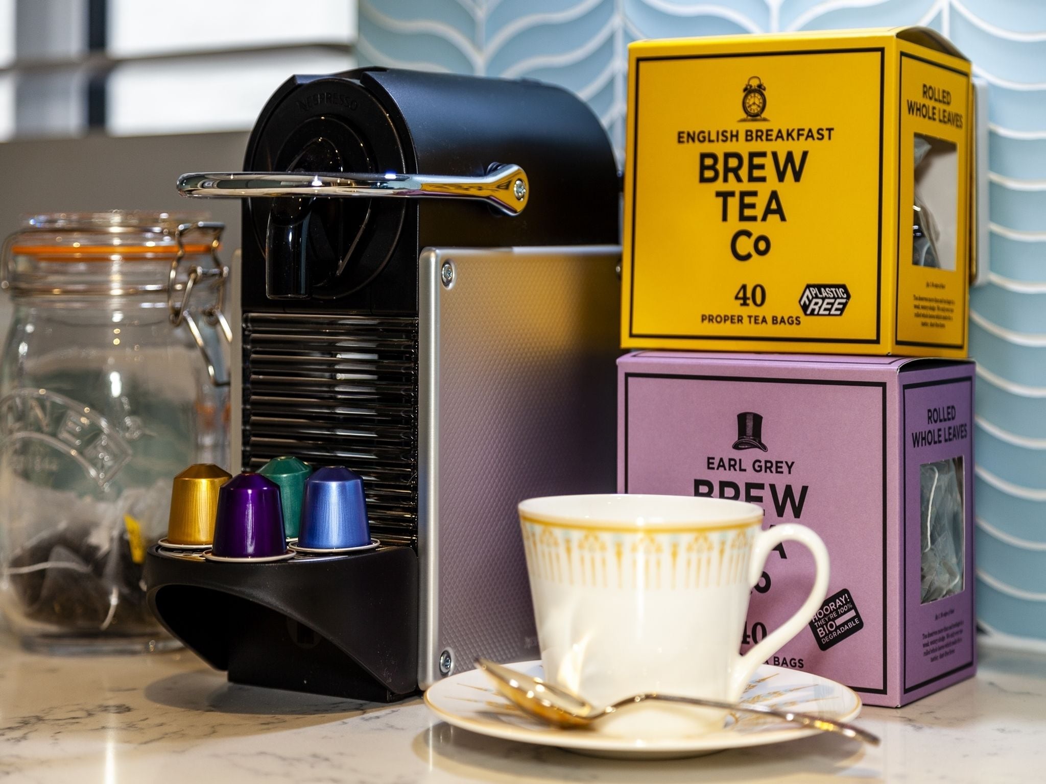 Una macchina del caffè, scatole di tè, una tazza e un cucchiaio su un piano di lavoro in cucina.