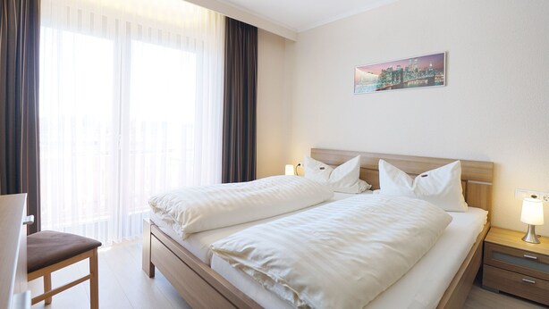A hotel room with two beds, a chair, a nightstand with a lamp, and a cityscape painting on the wall. - Im Gewölbe (Bad Fuessing)