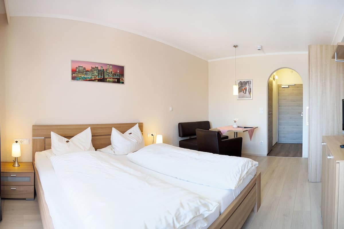 A hotel room with a large bed, bedside tables with lamps, a desk with a chair, a television, and a painting on the wall.