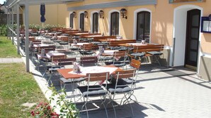 An outdoor dining area with multiple tables and chairs, a covered walkway, and a building with a sign that reads "Restaurant Zum Schöbel". - Im Gewölbe (Bad Fuessing)