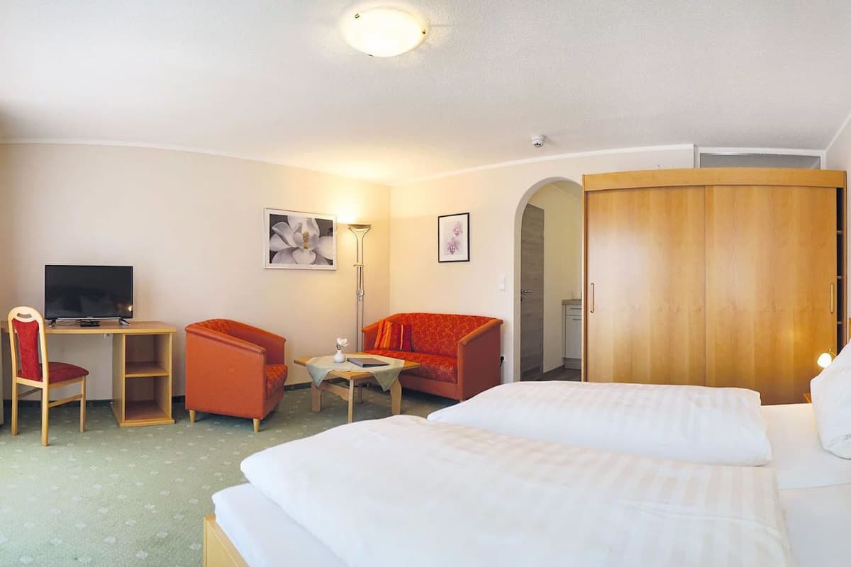 A hotel room with a bed, two chairs, a desk with a computer, a small table, and a wardrobe.