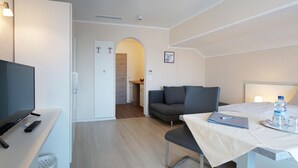 A modern hotel room with a flat-screen TV, a dining table with a water bottle, and a sofa. - Im Gewölbe (Bad Fuessing)