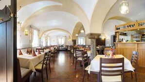 A restaurant with high arched ceilings, stone flooring, and tables set with white tablecloths and red napkins. - Im Gewölbe (Bad Fuessing)