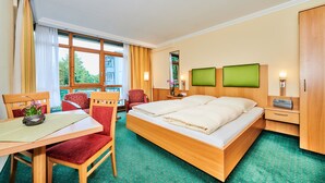 A hotel room with a large bed, a desk with a chair, a small table with a plant, and a wardrobe. - City Appartementhotel (Bad Fuessing)