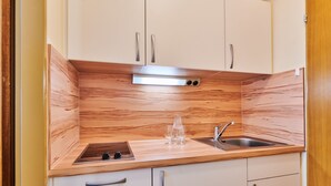 A compact kitchen with wooden cabinetry, a stainless steel sink, and a built-in range hood. - City Appartementhotel (Bad Fuessing)