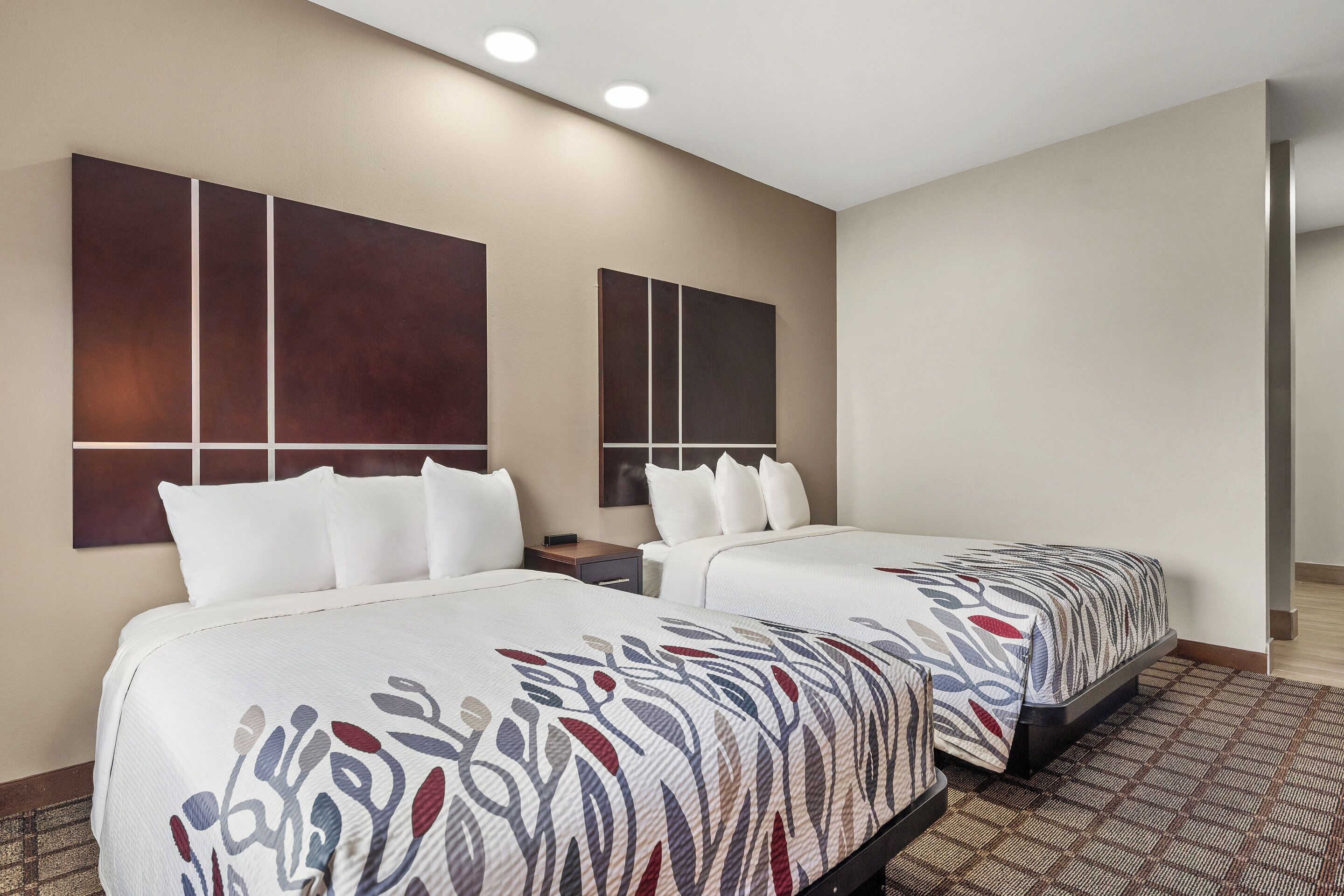 Quarto de hotel com duas camas, uma grande pintura abstrata na parede e um tapete estampado.