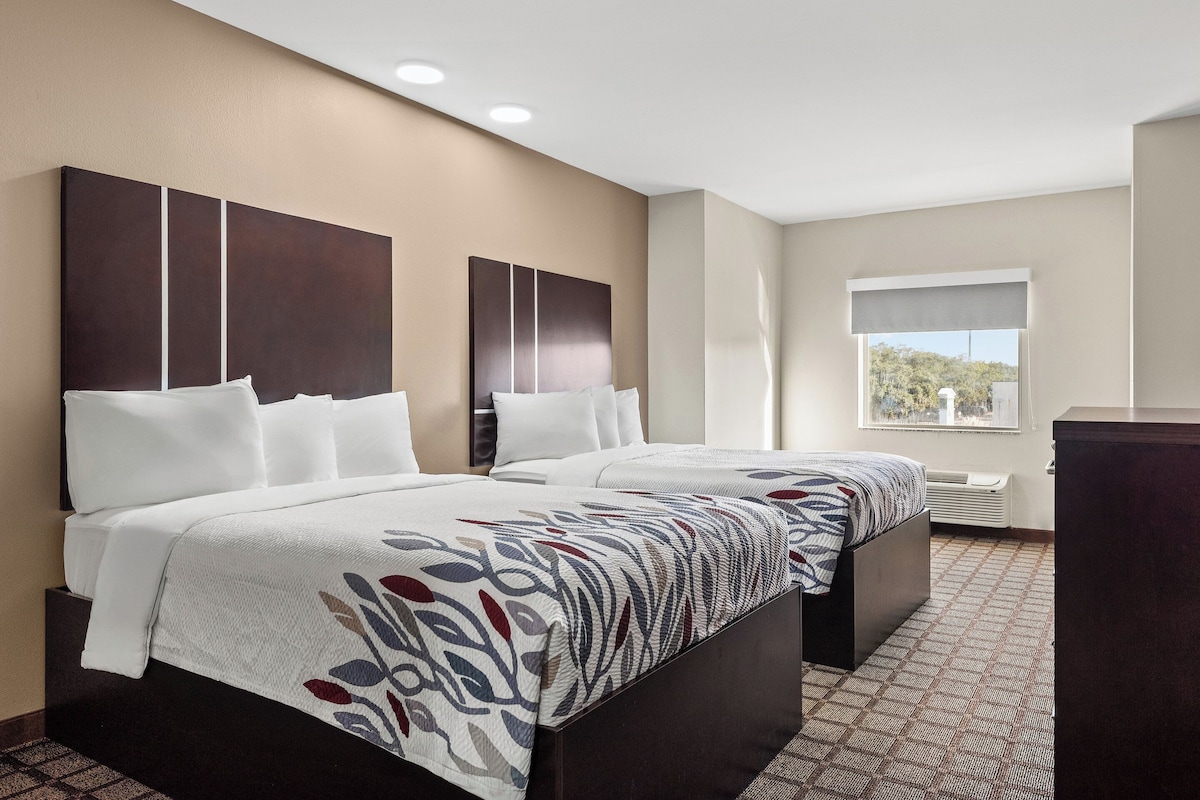 A hotel room with two beds, a large window, and a view of the outdoors.