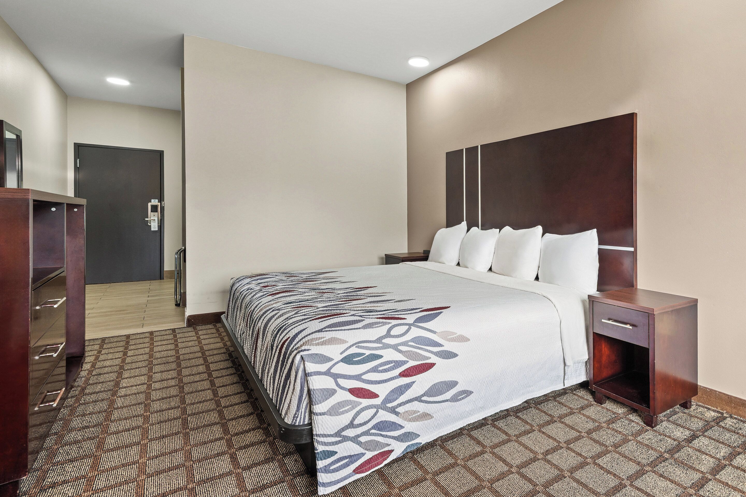 Una habitación de hotel con una cama grande, una mesita de noche de madera, un escritorio y una silla.