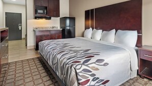 Une chambre d’hôtel dotée d’un grand lit, d’une tête de lit en bois, d’un four à micro-ondes encastré, d’un réfrigérateur et d’une petite kitchenette.