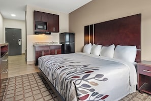 A hotel room with a large bed, a wooden headboard, a built-in microwave, a refrigerator, and a small kitchenette.
