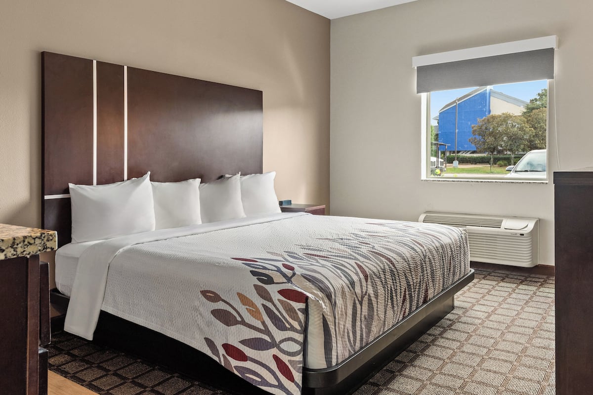 A hotel room with a large bed, a headboard, a window with a view of the outside, and a radiator.