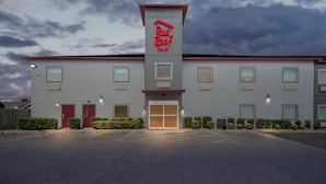 Un hôtel Red Roof Inn au design moderne, avec une entrée centrale dotée d’une porte en verre et d’une enseigne rouge sur le toit.