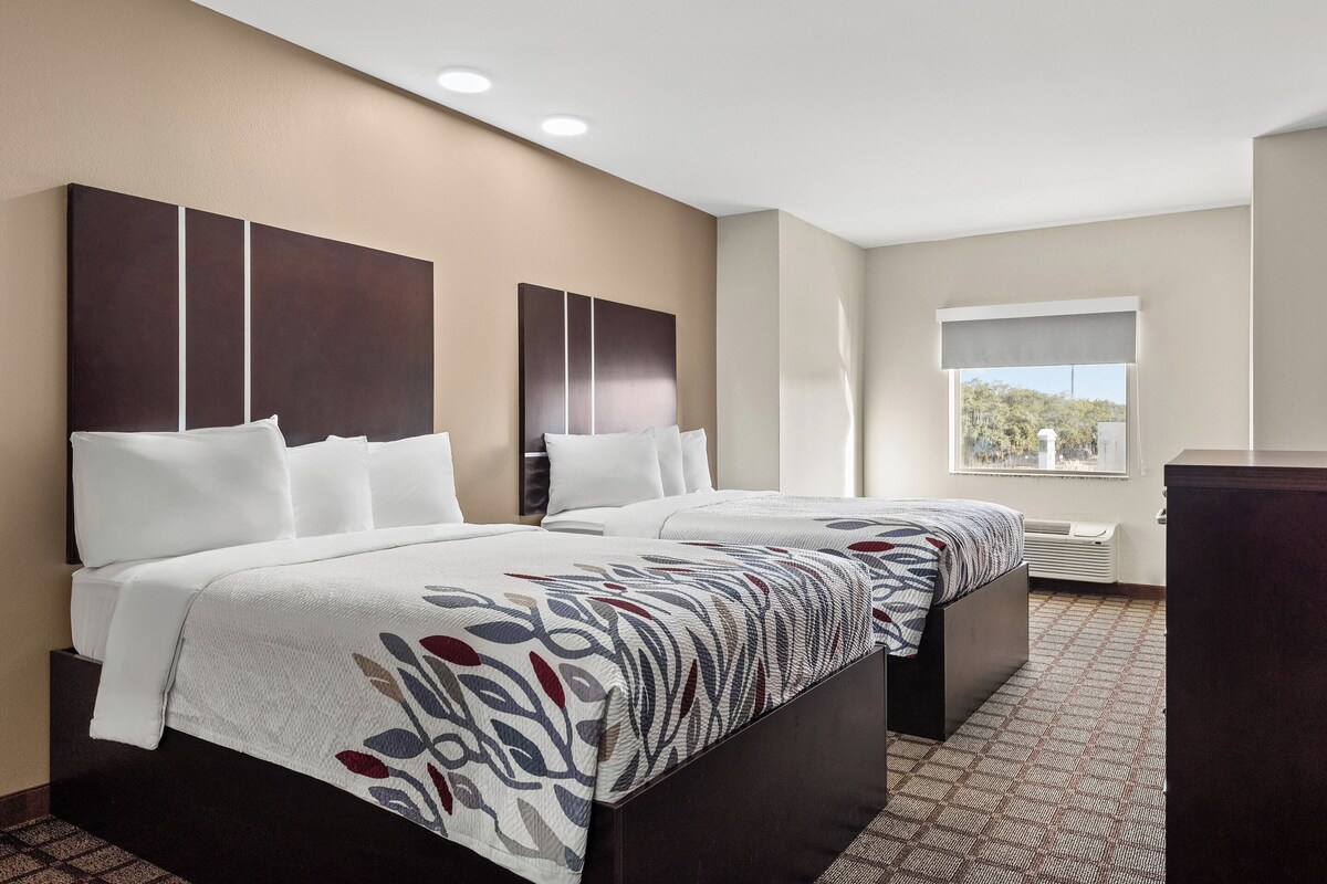 A hotel room with two beds, a large window, and a view of the outdoors.