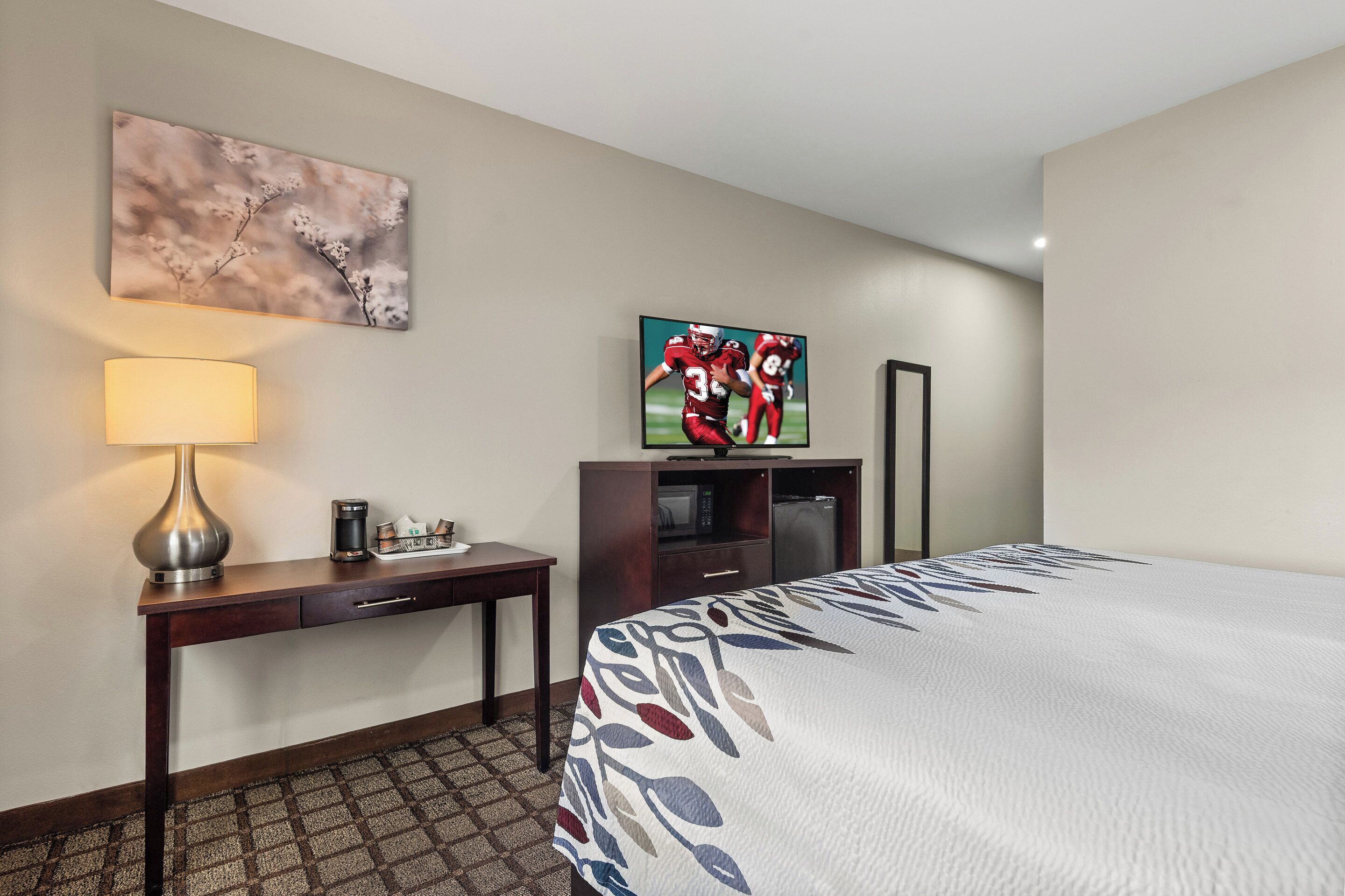 A hotel room with a bed, a desk with a lamp, a television, and a microwave.