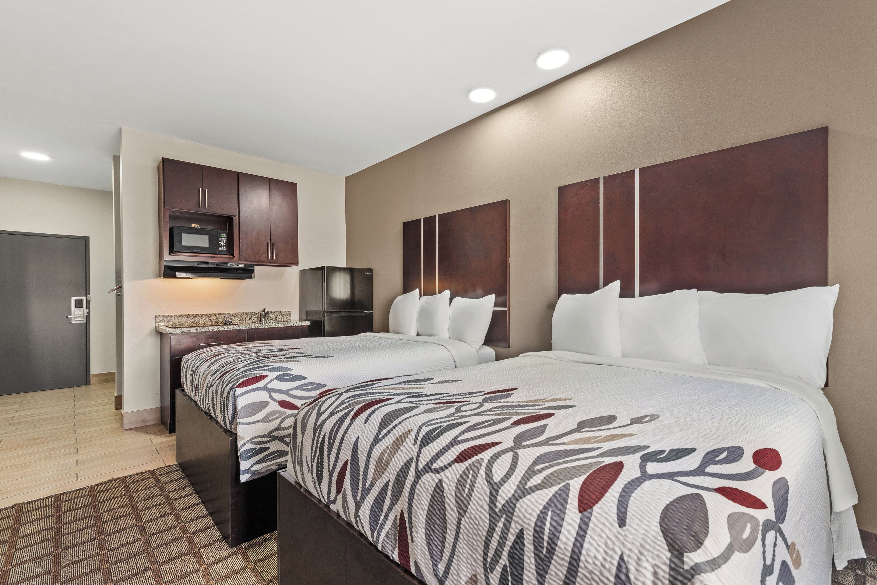 A hotel room with two beds, a kitchenette, and a large window.
