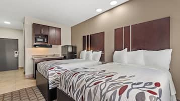 A hotel room with two beds, a kitchenette, and a large window.
