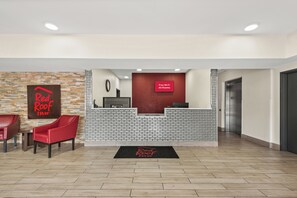 A Red Roof Inn reception area with a brick wall, a reception desk, and a digital sign indicating free Wi-Fi in all rooms.