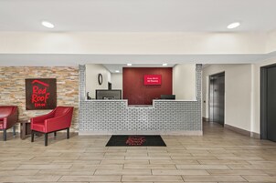 Zona de recepción de hotel con el letrero de Red Roof Inn, un mostrador de recepción, una pantalla digital y un área para la recepción.