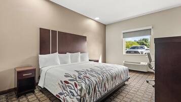 A hotel room with a large bed, a nightstand, a window with a view of a car, and an air conditioning unit.