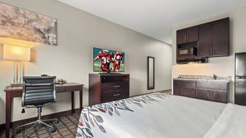 A hotel room with a bed, desk, chair, TV, microwave, and kitchenette.