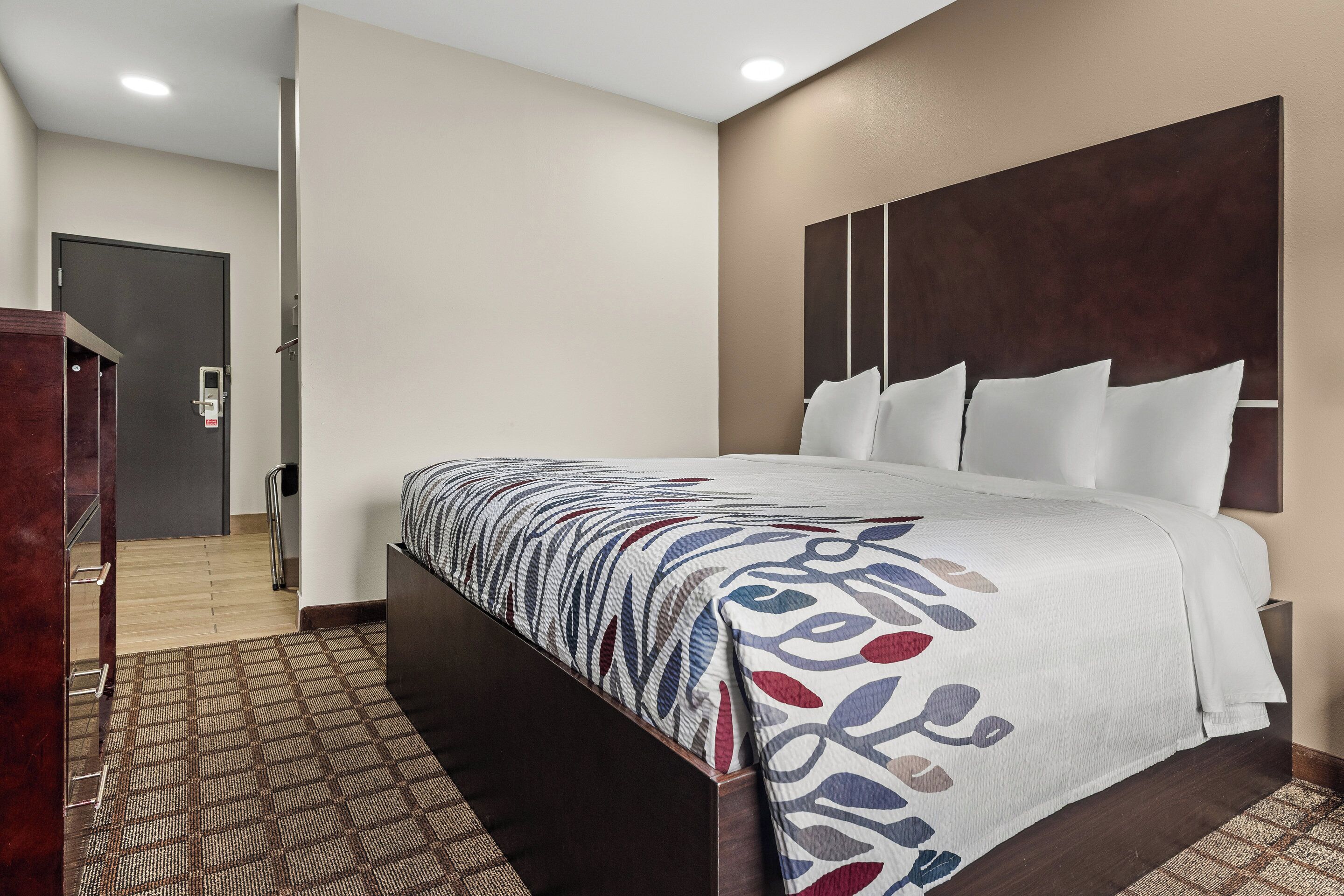 A hotel room with a large bed, a wooden headboard, and a patterned rug.
